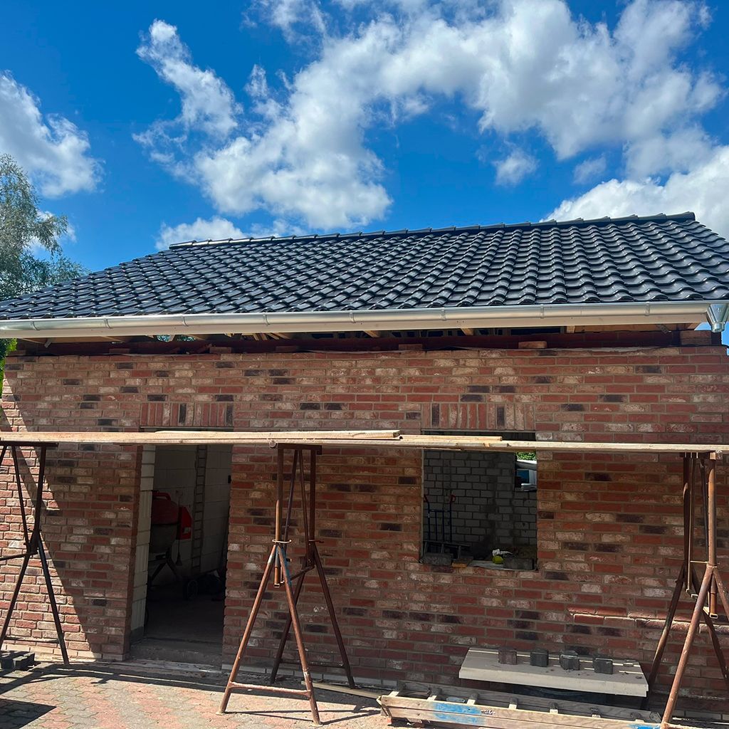 Ansicht eines Hauses im Bau mit Ziegelfassade und Dachdeckung unter blauem Himmel